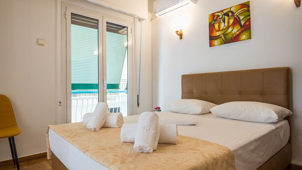 A hotel room with a bed, a chair, a painting, and a balcony. - Victoria Best Apartment (Athens)