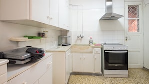 A compact kitchen with white cabinets, a built-in oven, and a stainless steel range hood. - Victoria Best Apartment (Athens)