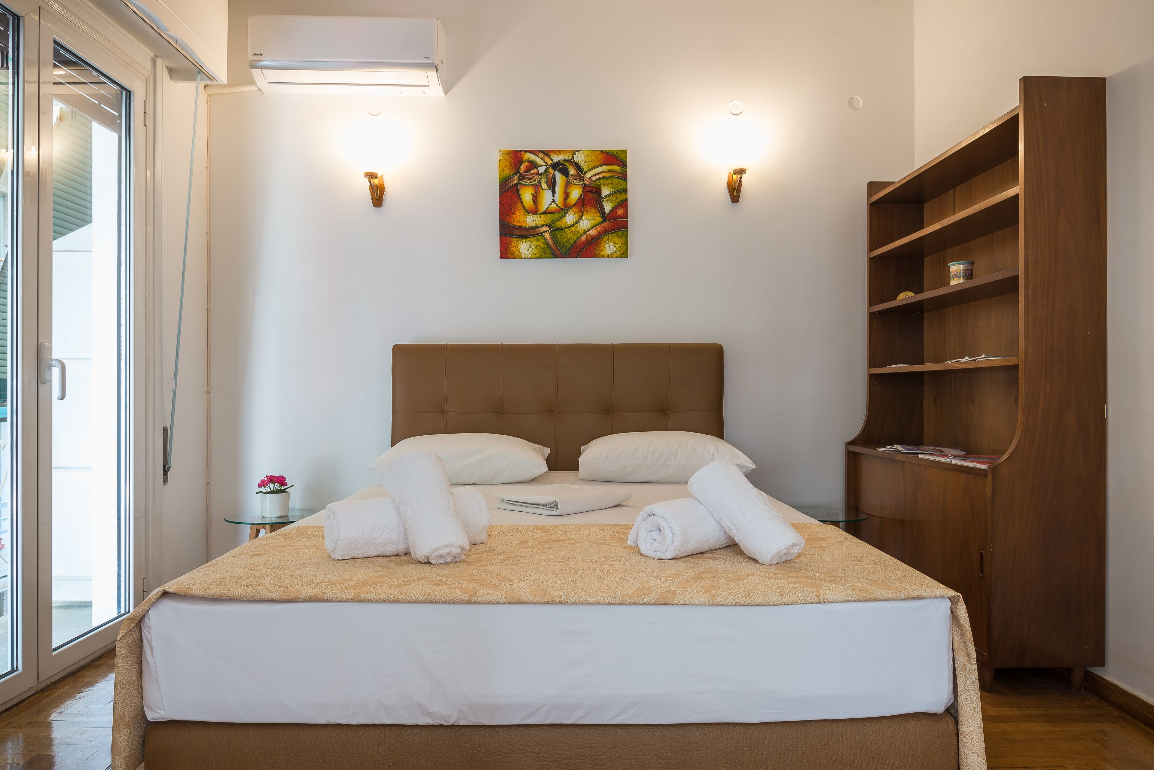 Un lit bien fait, avec du linge de lit blanc et des serviettes pliées, une tête de lit en bois, un tableau accroché au mur et une armoire en bois.