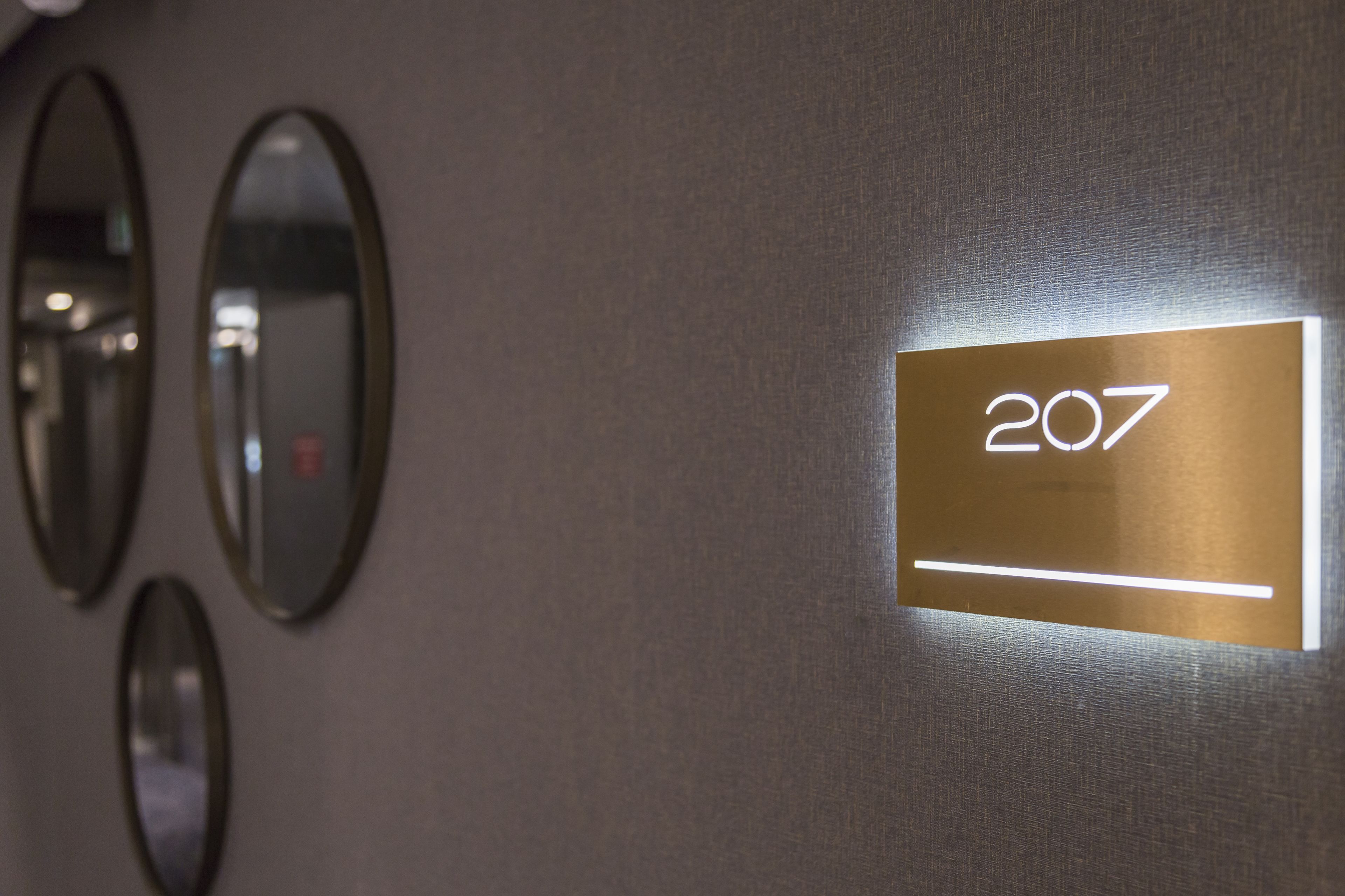 A wall with three oval mirrors and a sign displaying the number 207.