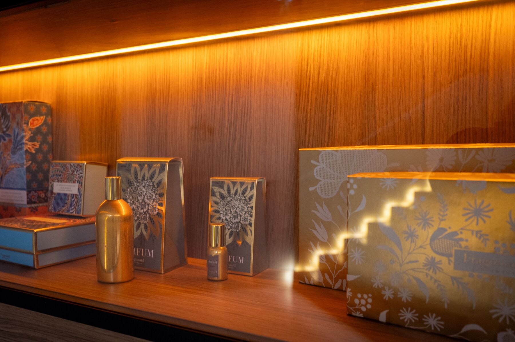 Une collection de boîtes et de flacons de parfum est exposée sur une étagère en bois.