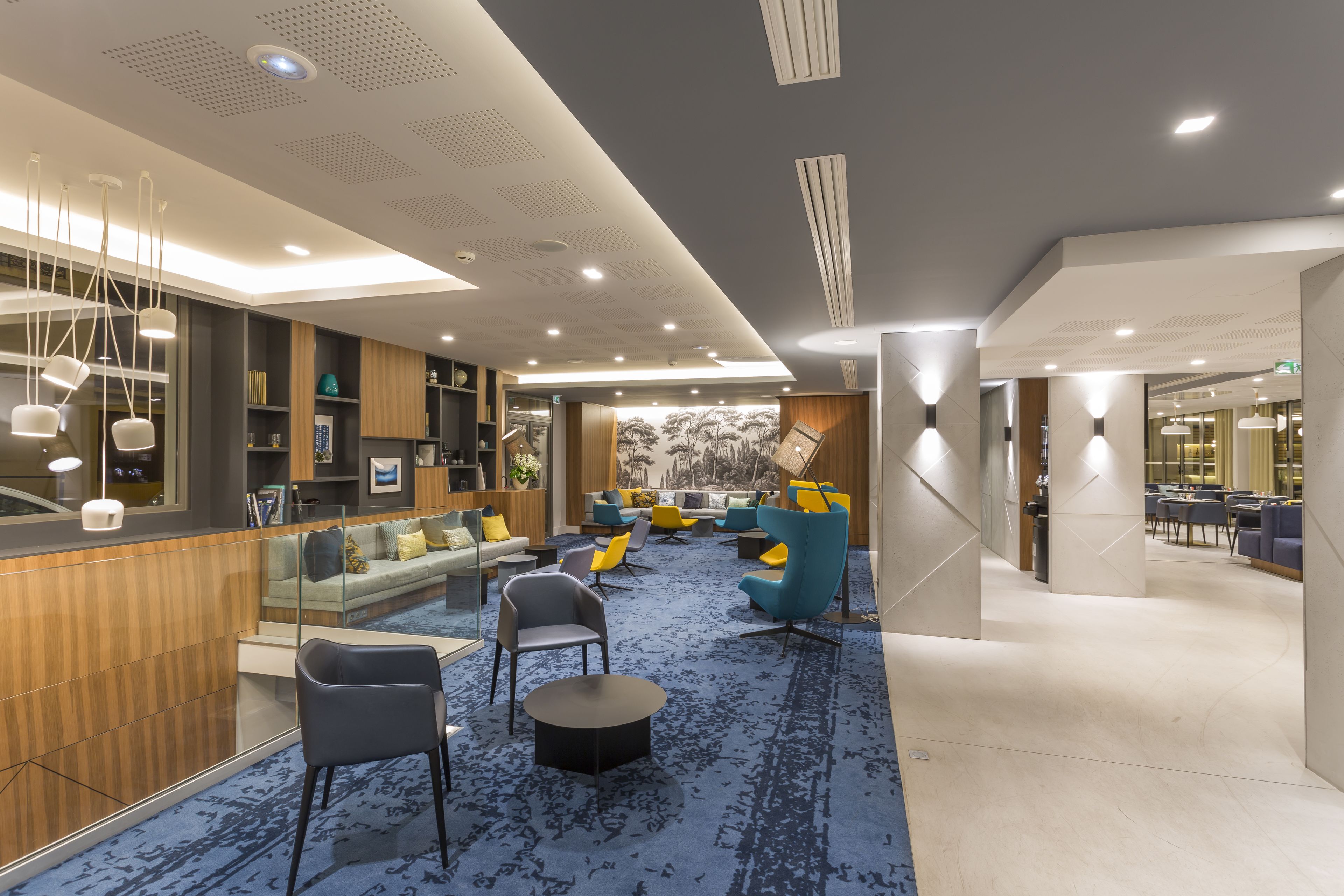 Un espace de détente moderne avec un tapis bleu, des sièges confortables et un bar agrémenté d’éléments en bois.