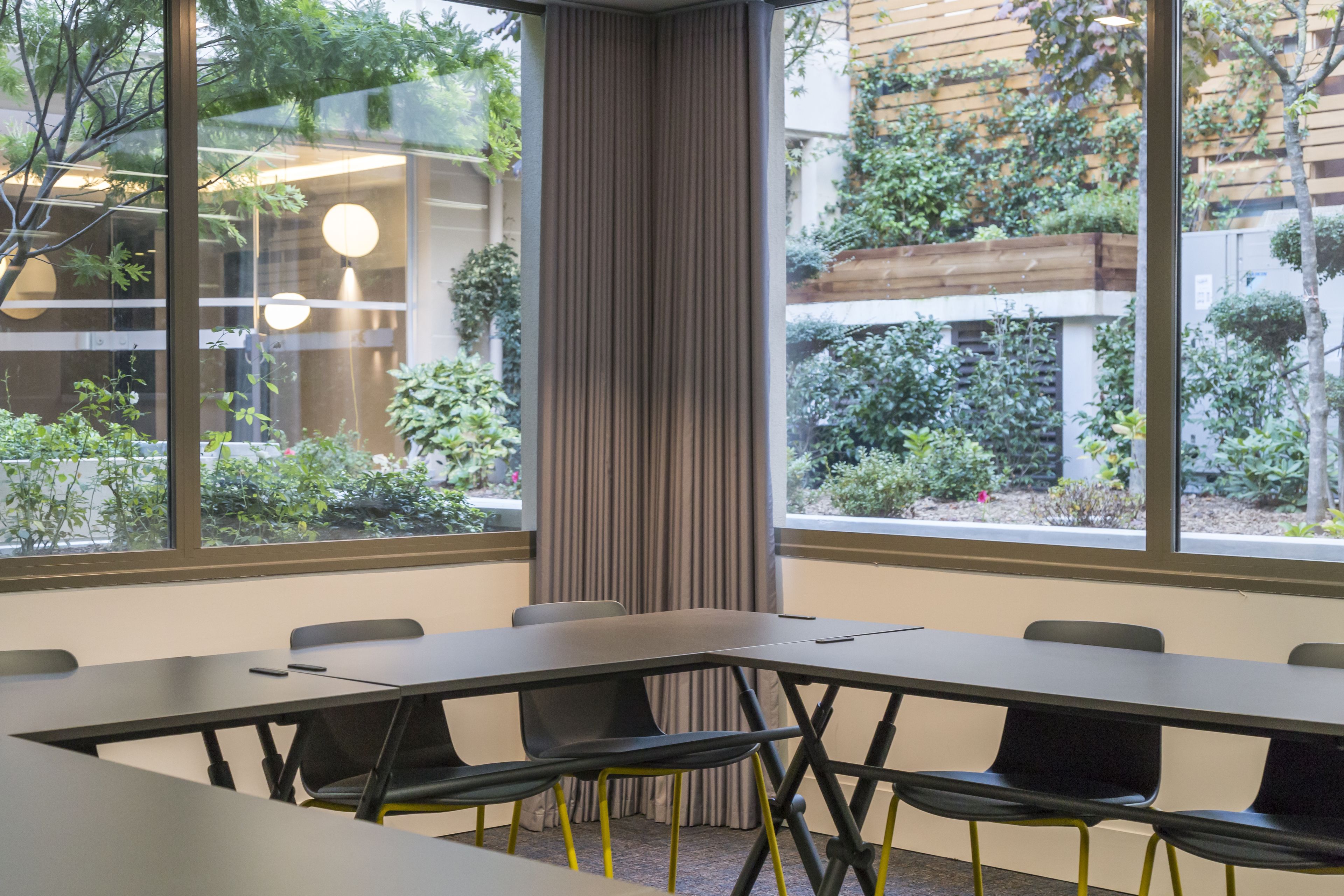 A conference room with a long table and chairs, large windows with a view of greenery, and a curtain divider.