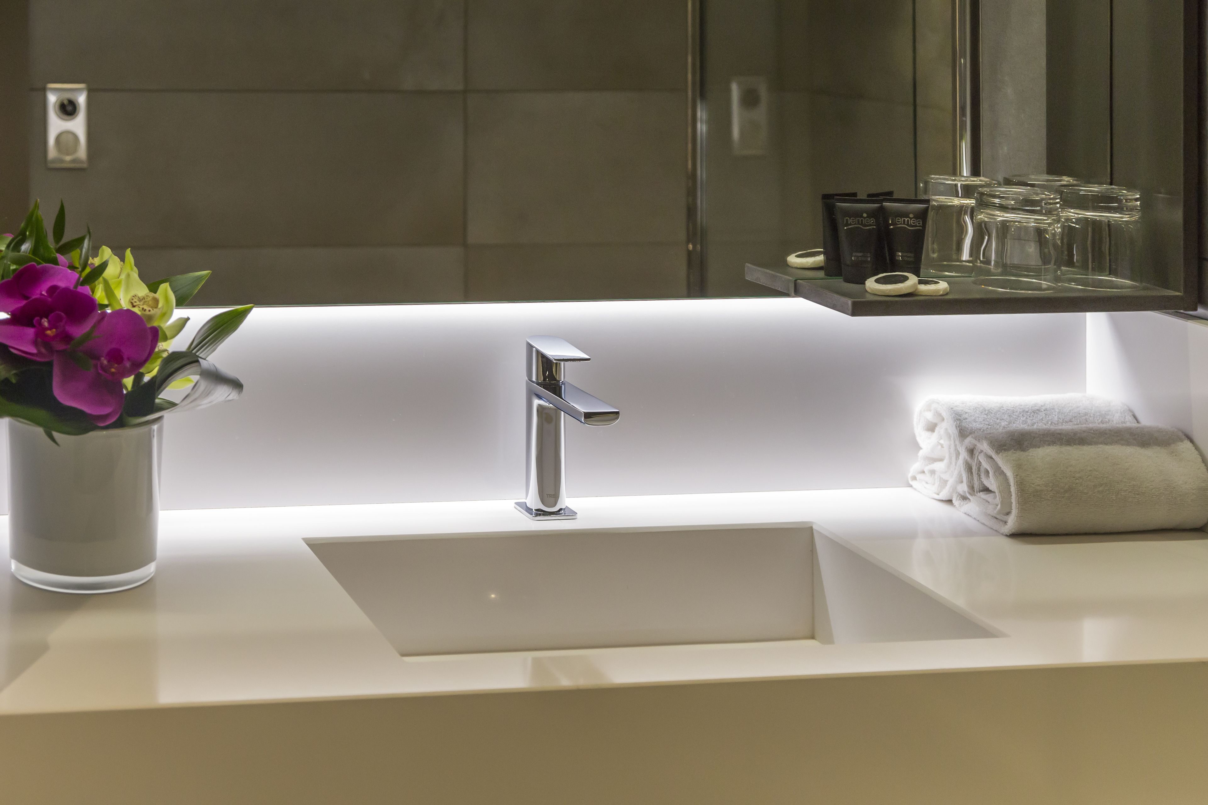 A modern bathroom with a white sink, a chrome faucet, and a glass vase with purple flowers.