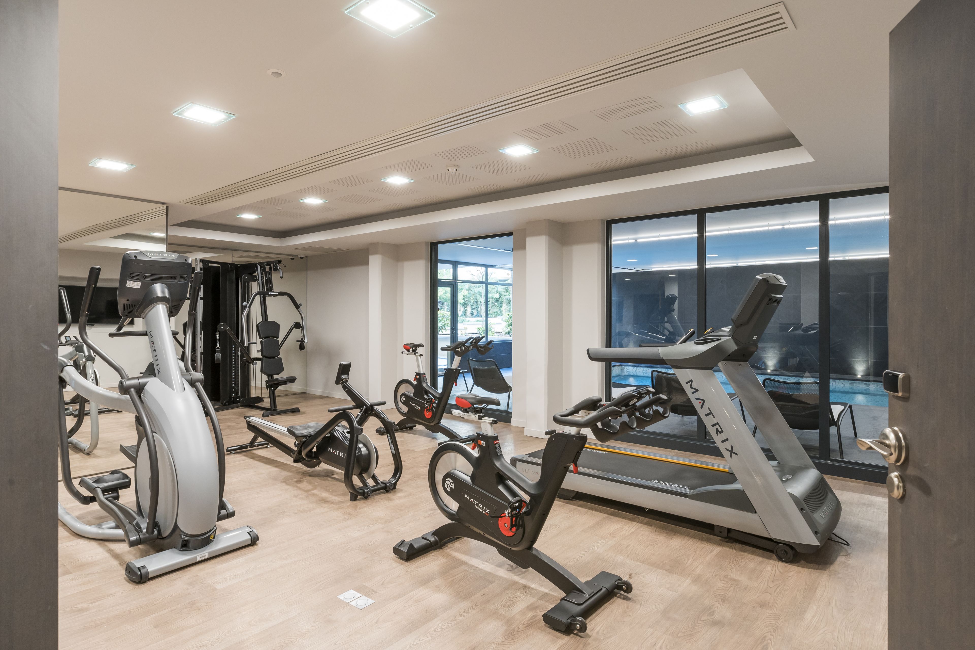 Un gimnasio moderno con diversas máquinas de cardio, amplias ventanas y un interior limpio y bien iluminado.