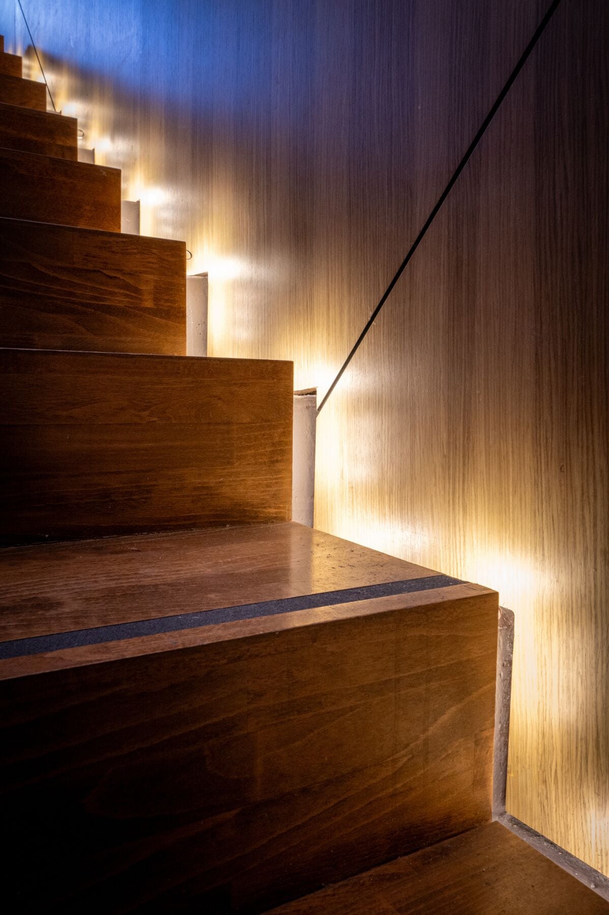 Una escalera de madera de diseño moderno, con barandilla recta y escalones iluminados.