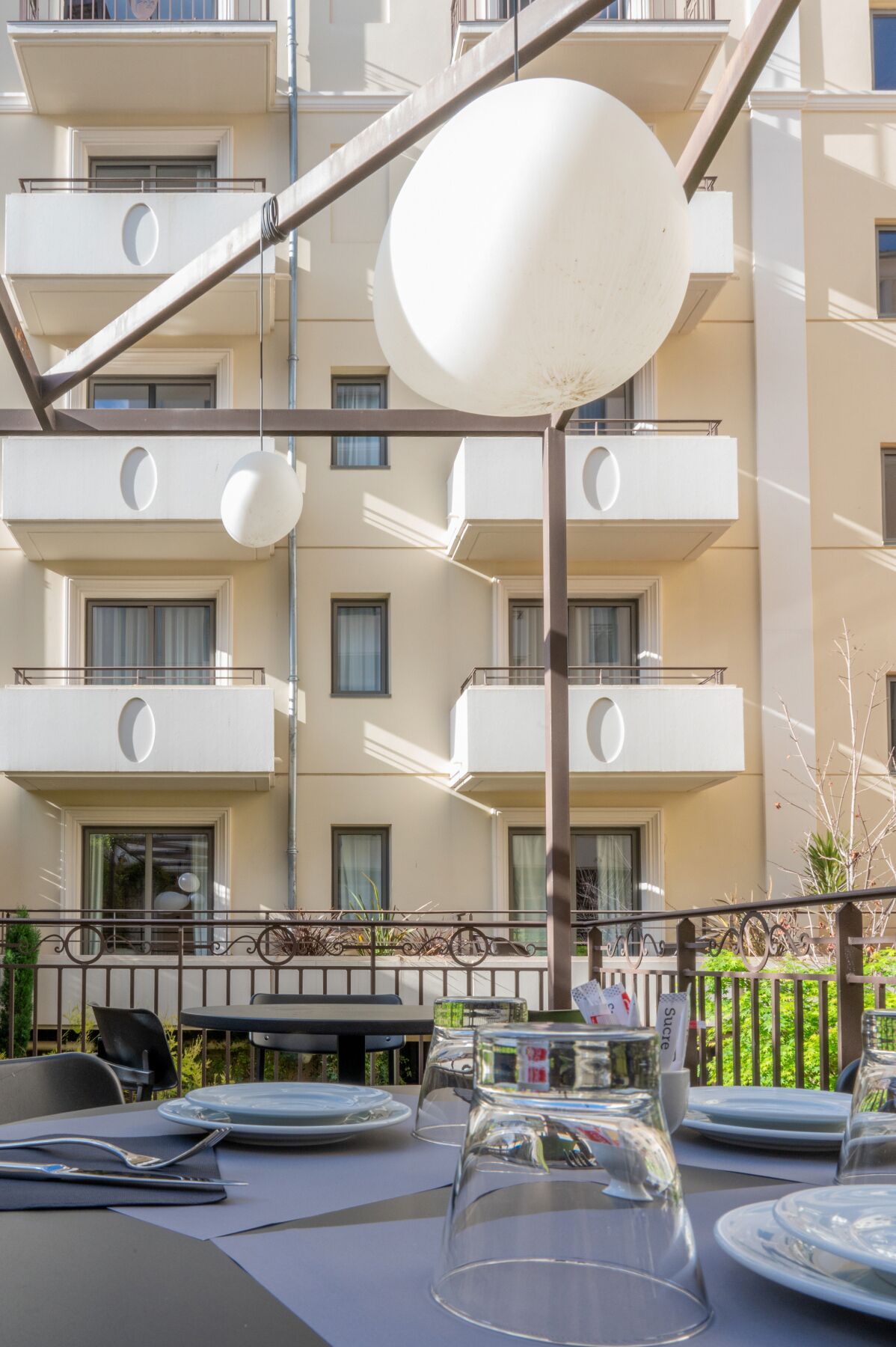 Un espace repas avec des tables préparées pour deux personnes, des sièges en plein air et une vue sur un immeuble à plusieurs étages doté de balcons.