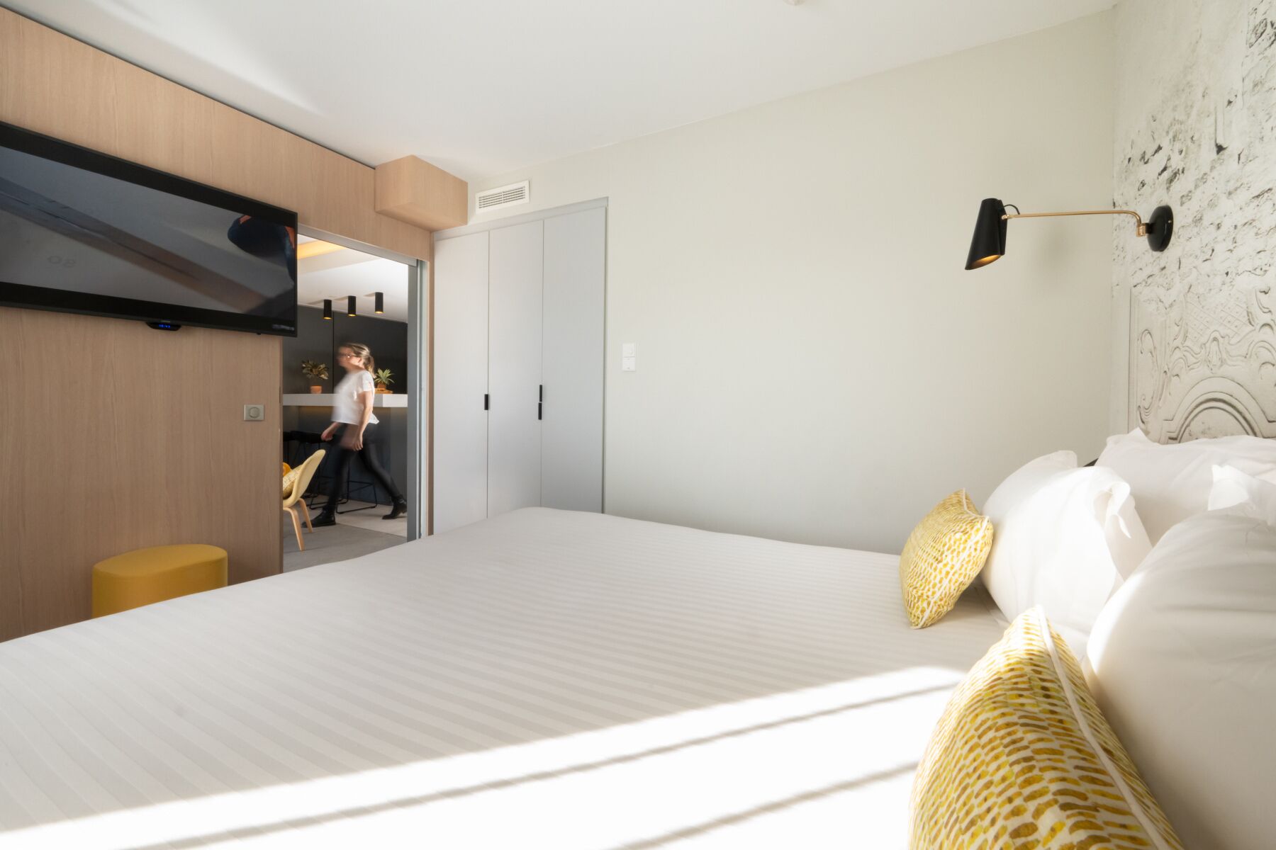 A modern bedroom with a large bed, a wardrobe, a desk, and a lamp.