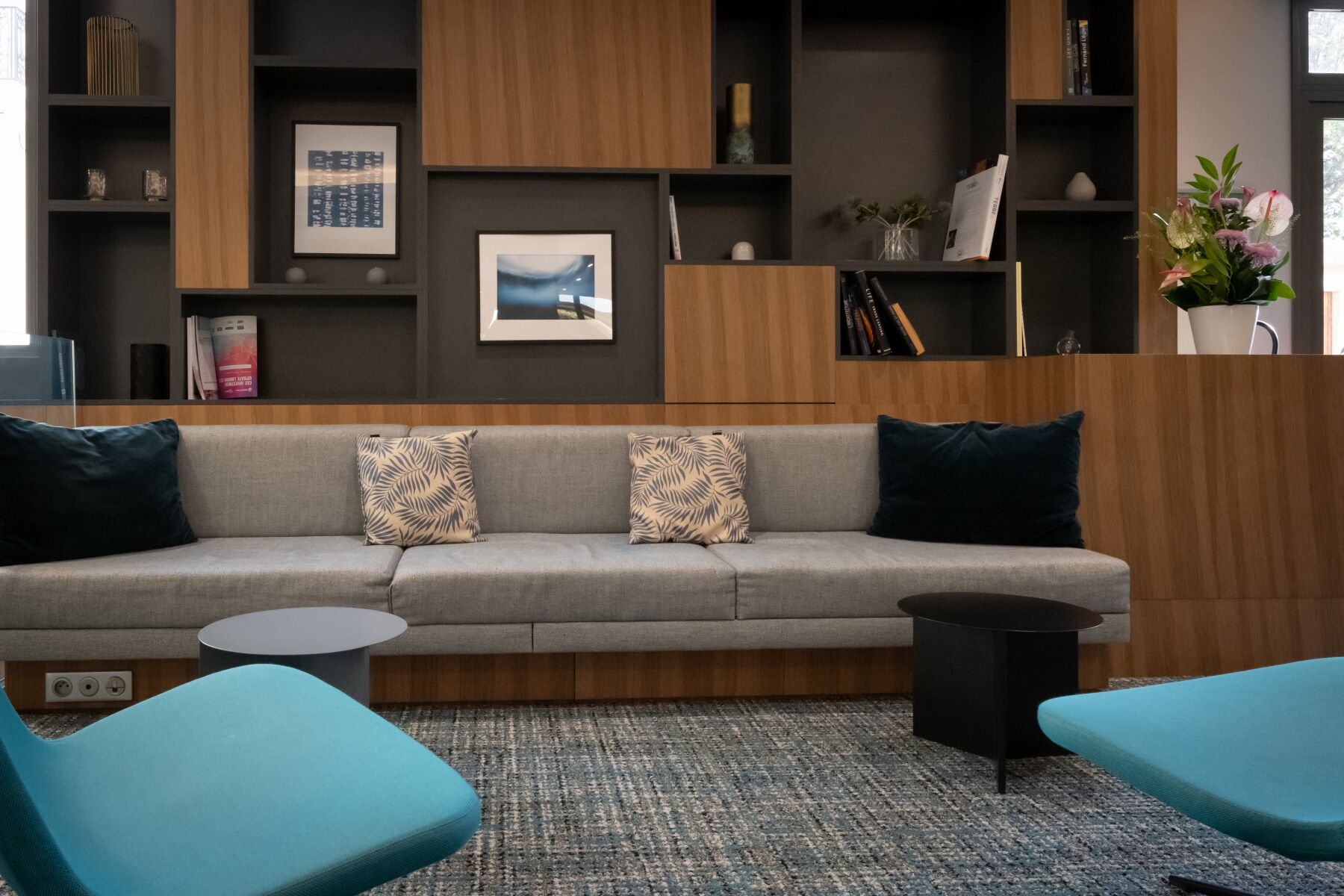 Uma sala de estar moderna com um sofá cinzento, duas poltronas azul-esverdeadas, uma pequena mesa lateral preta e um tapete estampado.
