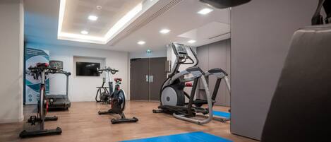 Een sportschool met loopbanden, hometrainers en matten.