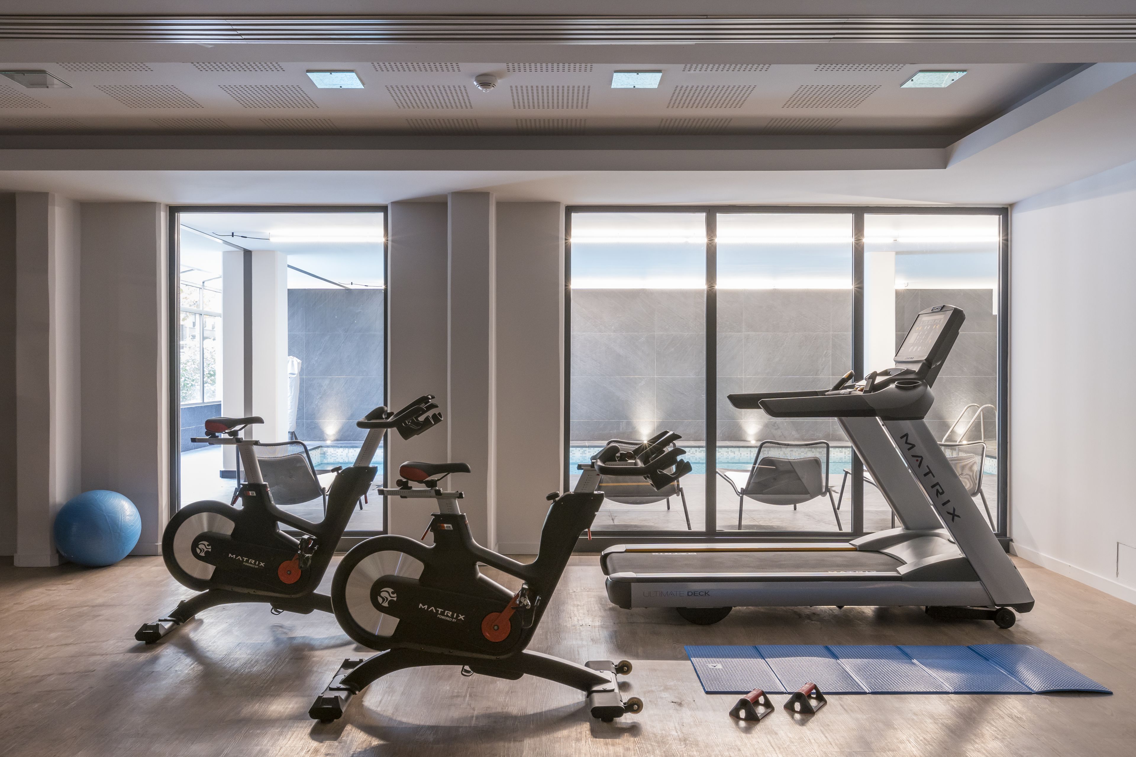 Un gimnasio moderno con dos bicicletas estáticas, una cinta de correr y pelotas de ejercicio.