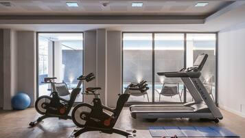 Un gimnasio moderno con dos bicicletas estáticas, una cinta de correr y pelotas de ejercicio.