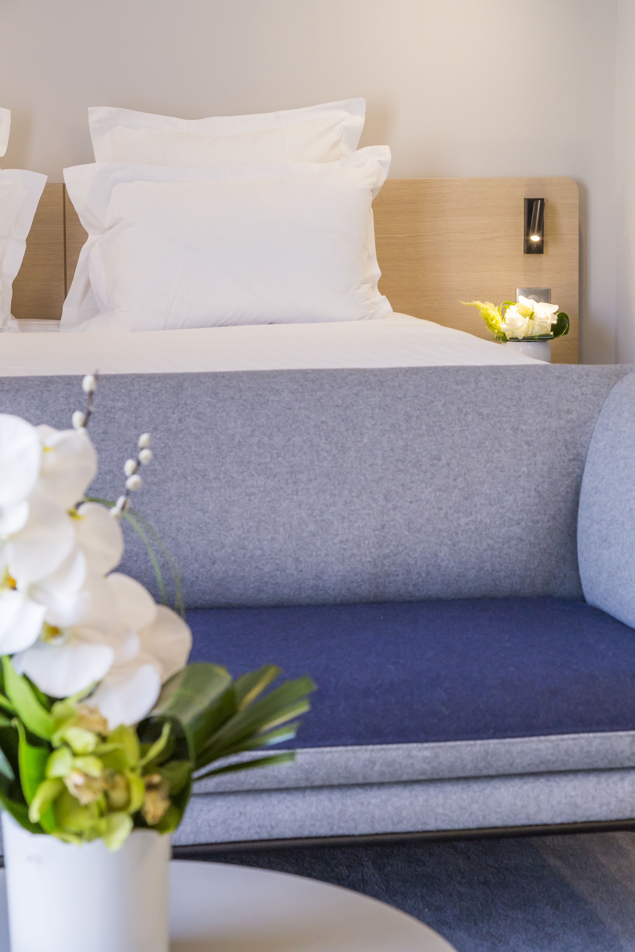 A modern hotel room with a bed, a sofa, and a nightstand with a lamp.