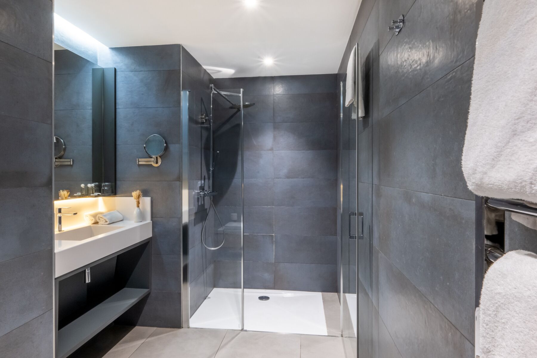 A modern bathroom with a glass-enclosed shower, a vanity with a mirror, and a towel rack.