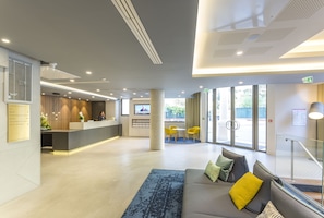 A modern lobby with a reception desk, seating area, and large windows. - Nemea Appart Hotel Cannes Palais (Cannes)