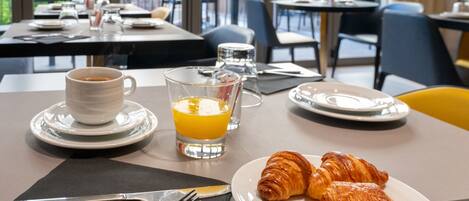A breakfast setting with croissants, a cup of coffee, and a glass of orange juice on a table.