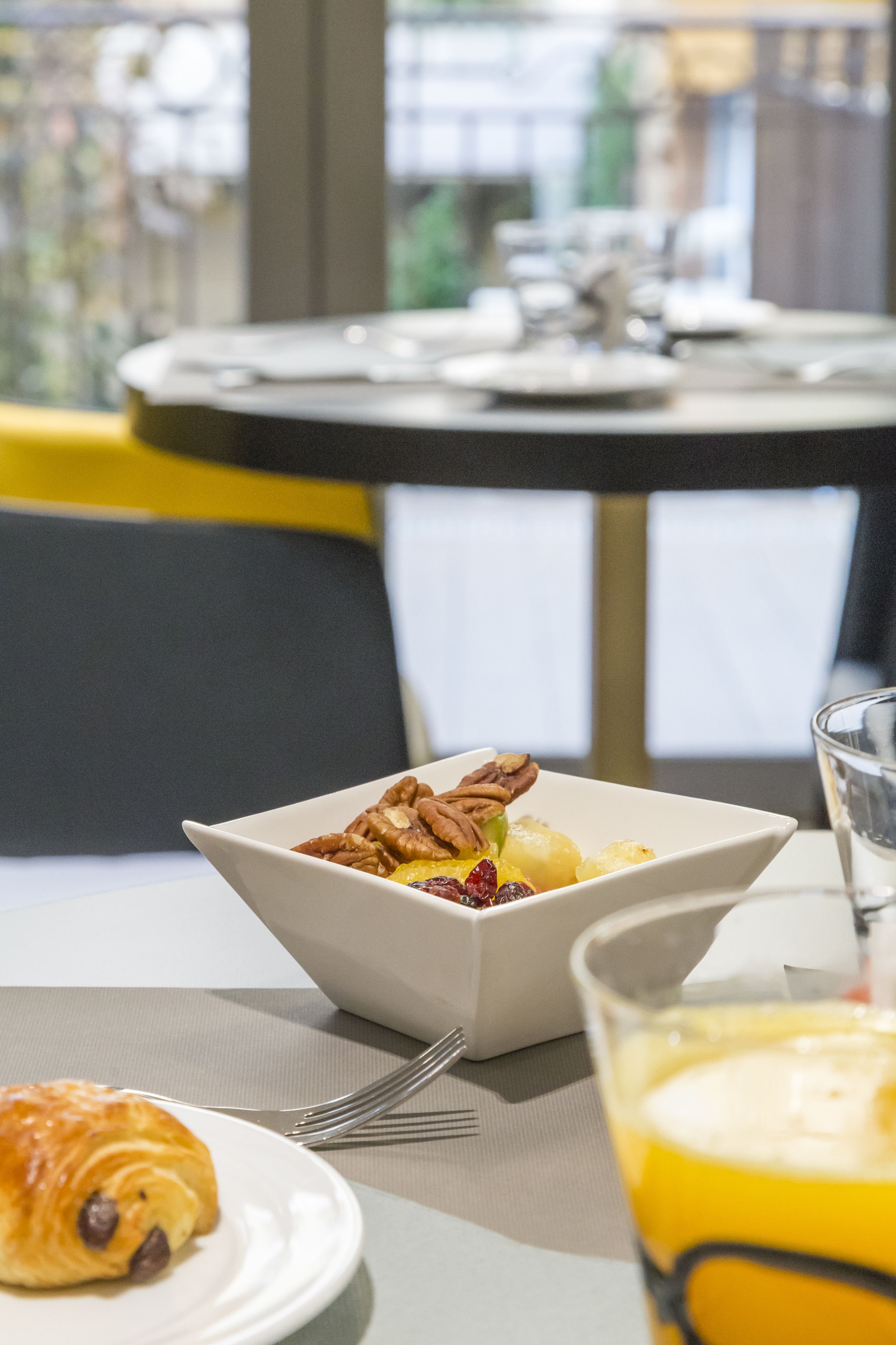A breakfast setting with a bowl of fruit and nuts, a croissant, and a glass of orange juice on a table.