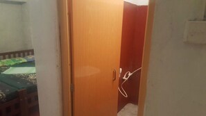 A room with a wooden door, a bed with patterned bedding, and a visible electrical cord.