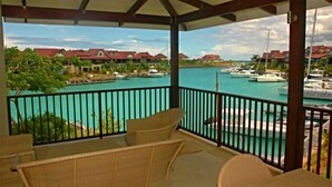 A covered balcony with wicker furniture overlooking a marina with boats and houses in the background. -  Eden Island, Beach front, Luxury, 3 Bed Ensuite, WiFi (Mahé Island)