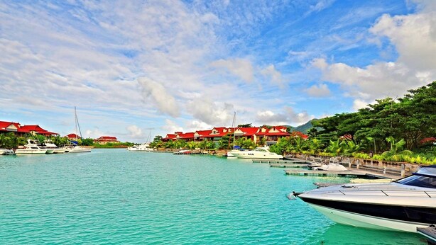 A marina with several boats docked, surrounded by buildings with red roofs and lush greenery. -  Eden Island, Beach front, Luxury, 3 Bed Ensuite, WiFi (Mahé Island)