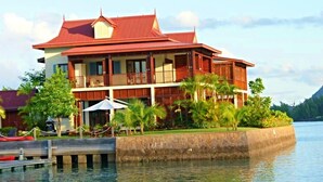 A two-story building with a red roof, multiple balconies, and a waterfront view. -  Eden Island, Beach front, Luxury, 3 Bed Ensuite, WiFi (Mahé Island)