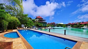 A swimming pool with a wooden deck, surrounded by lush greenery and a view of a marina with boats. -  Eden Island, Beach front, Luxury, 3 Bed Ensuite, WiFi (Mahé Island)