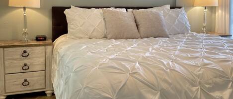 A neatly made bed with a white duvet, two bedside tables with lamps, and three wall-mounted paintings.