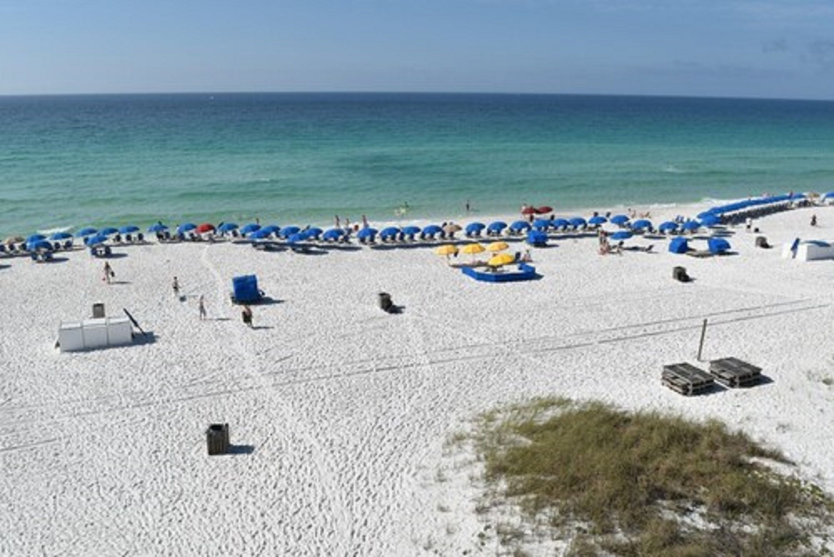 A beach with white sand, blue umbrellas, and a clear blue sky.