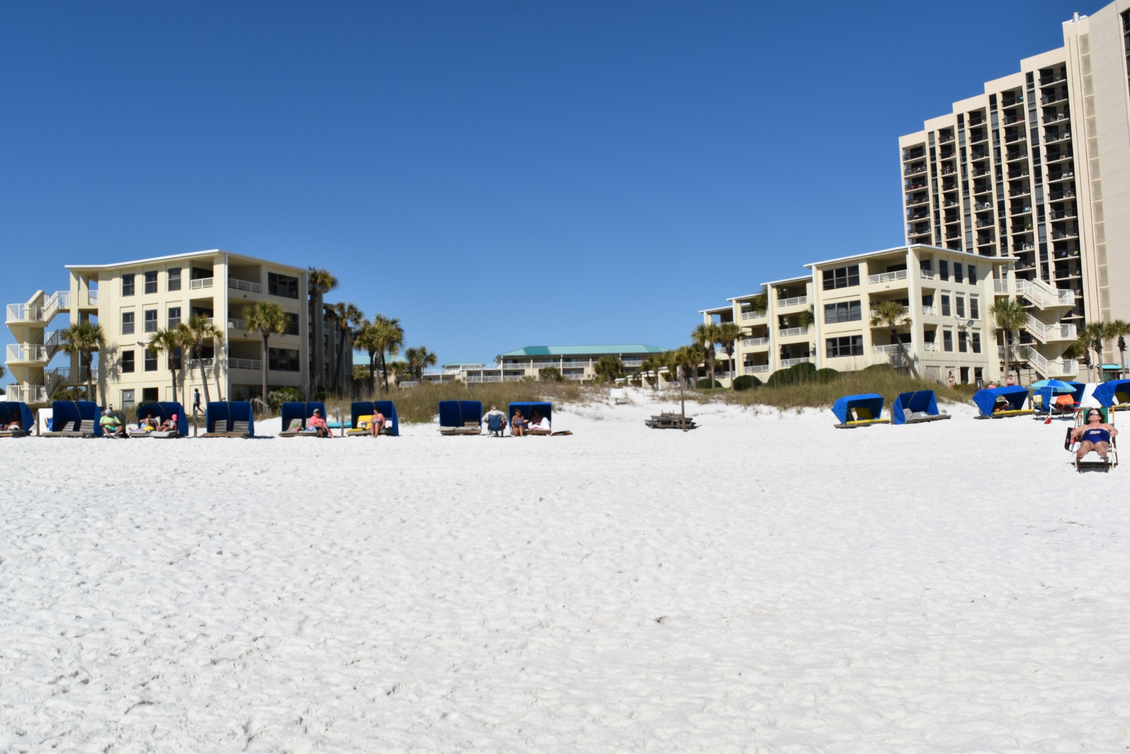 A beachfront hotel with multiple floors, beach umbrellas, and palm trees.