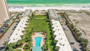 Vista aérea de un hotel con piscina central, rodeado por un estacionamiento y una playa.