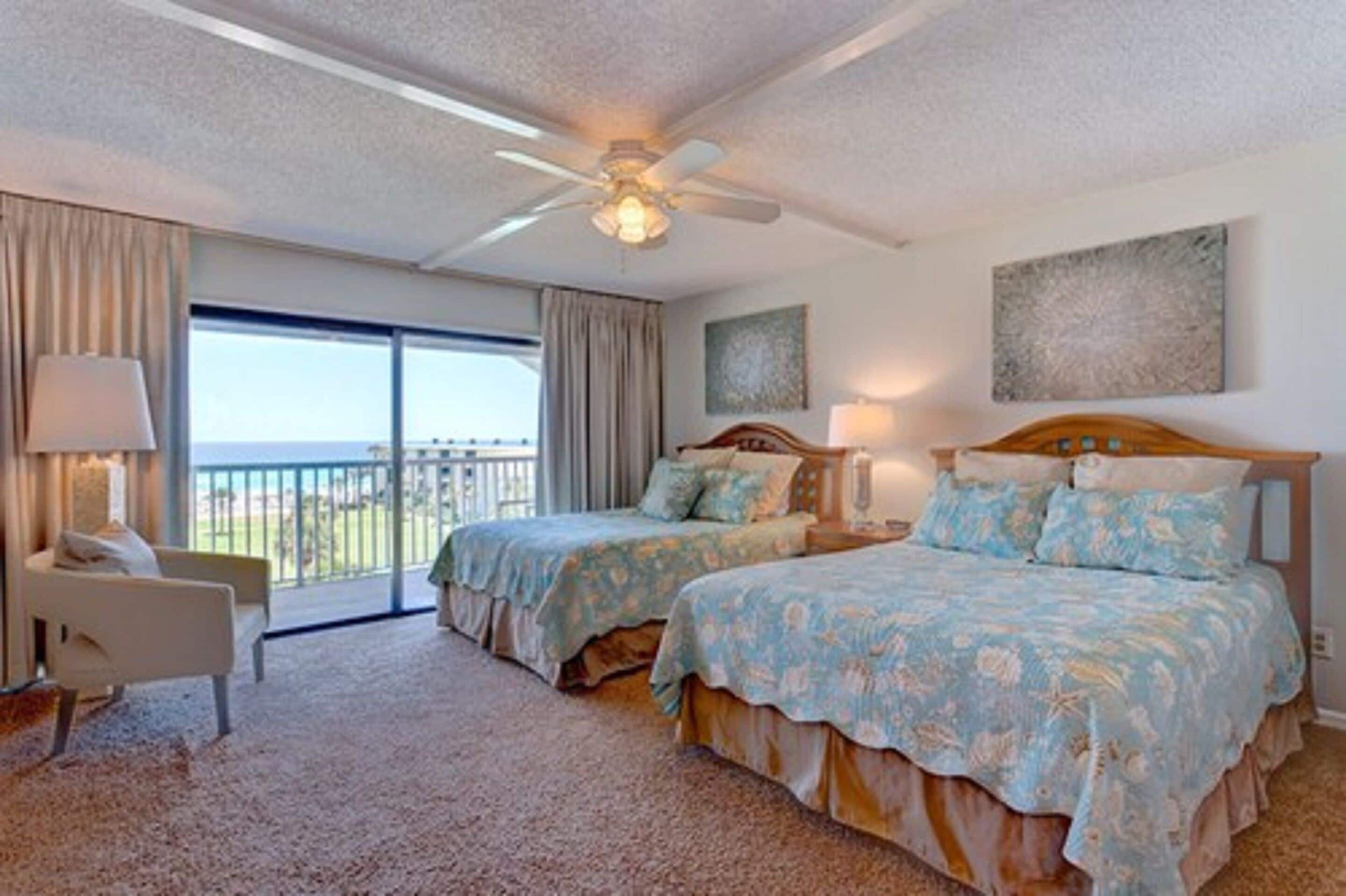 A hotel room with two beds, a balcony, a ceiling fan, and artwork on the walls.