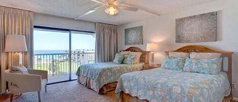 A hotel room with two beds, a balcony, a ceiling fan, and artwork on the walls.
