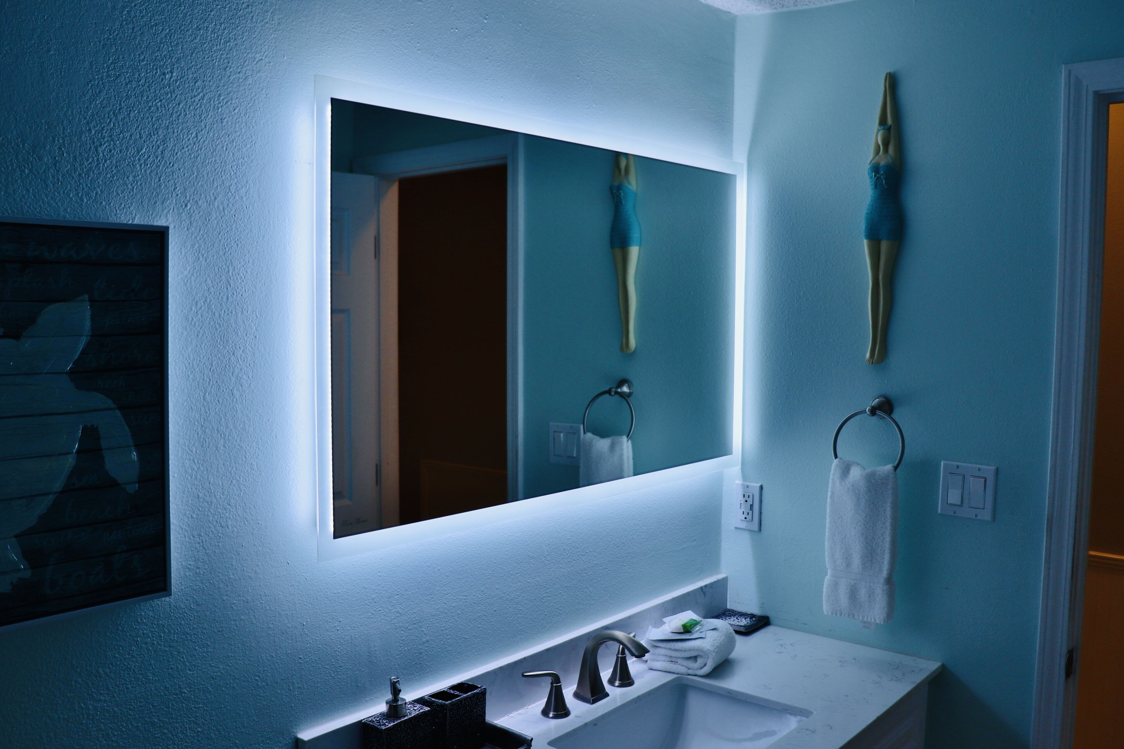 A bathroom with a large mirror, a white sink, and two towel rings.