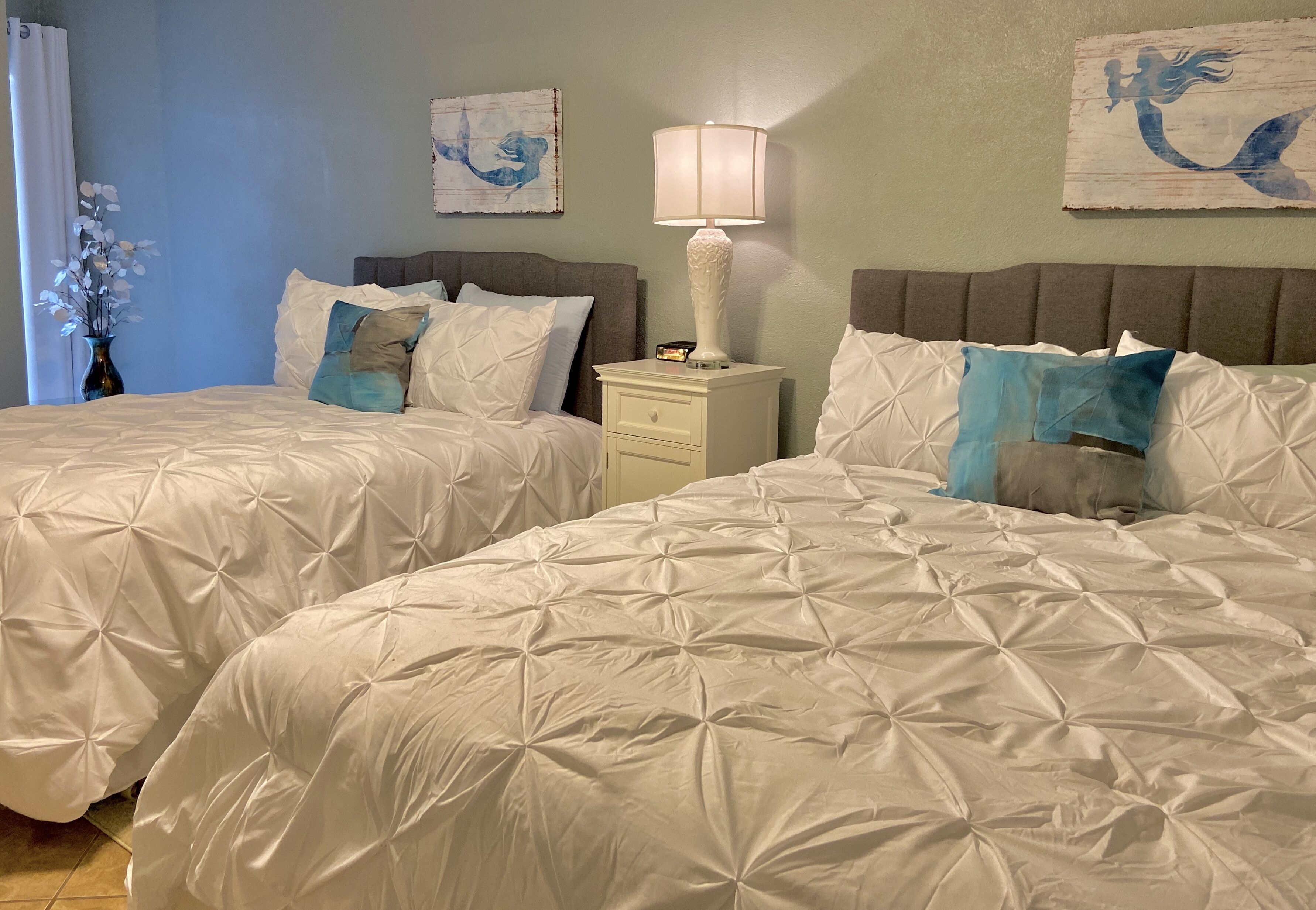 A hotel room with two beds, a nightstand, a lamp, and artwork on the walls.