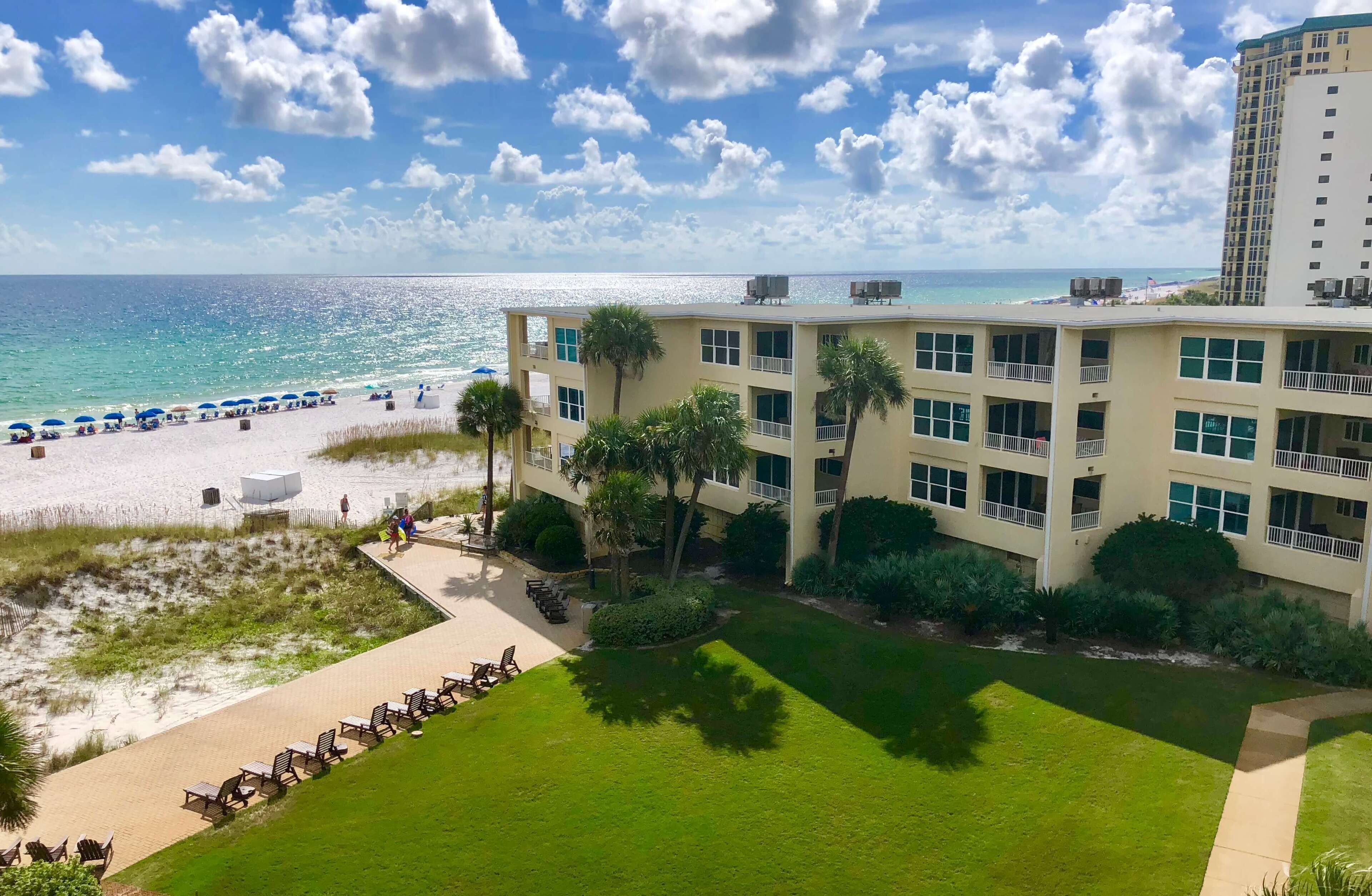 A hotel with a beach view, multiple floors, and a well-maintained lawn.