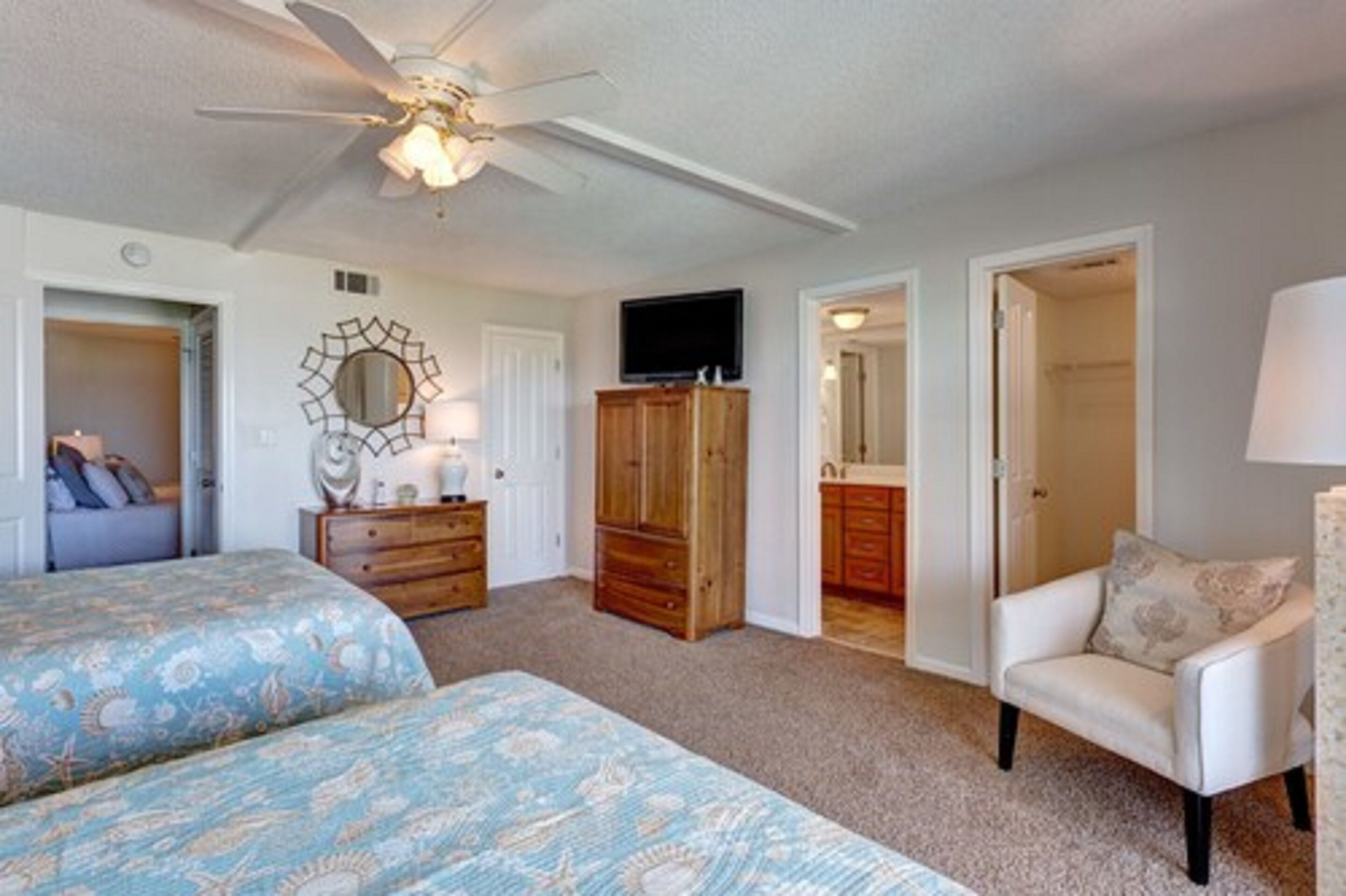 A bedroom with two beds, a ceiling fan, a TV, wooden cabinets, and a chair.