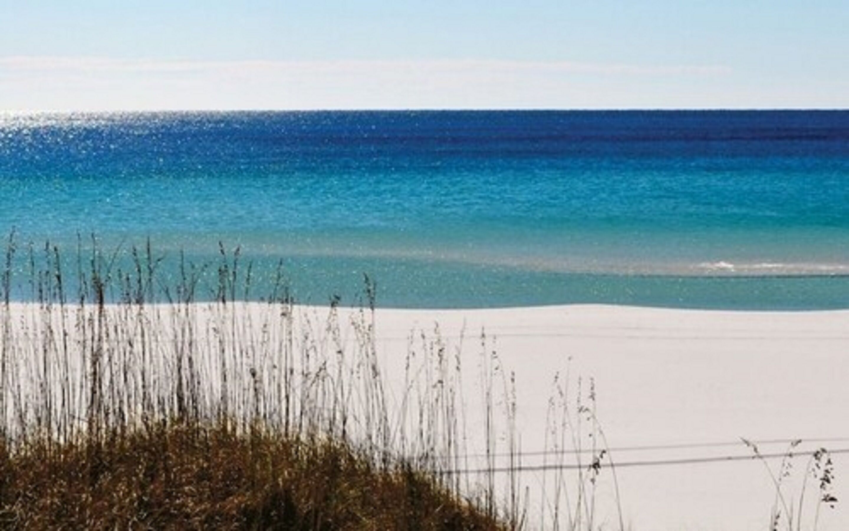 Een strand met helderblauw water en wit zand.