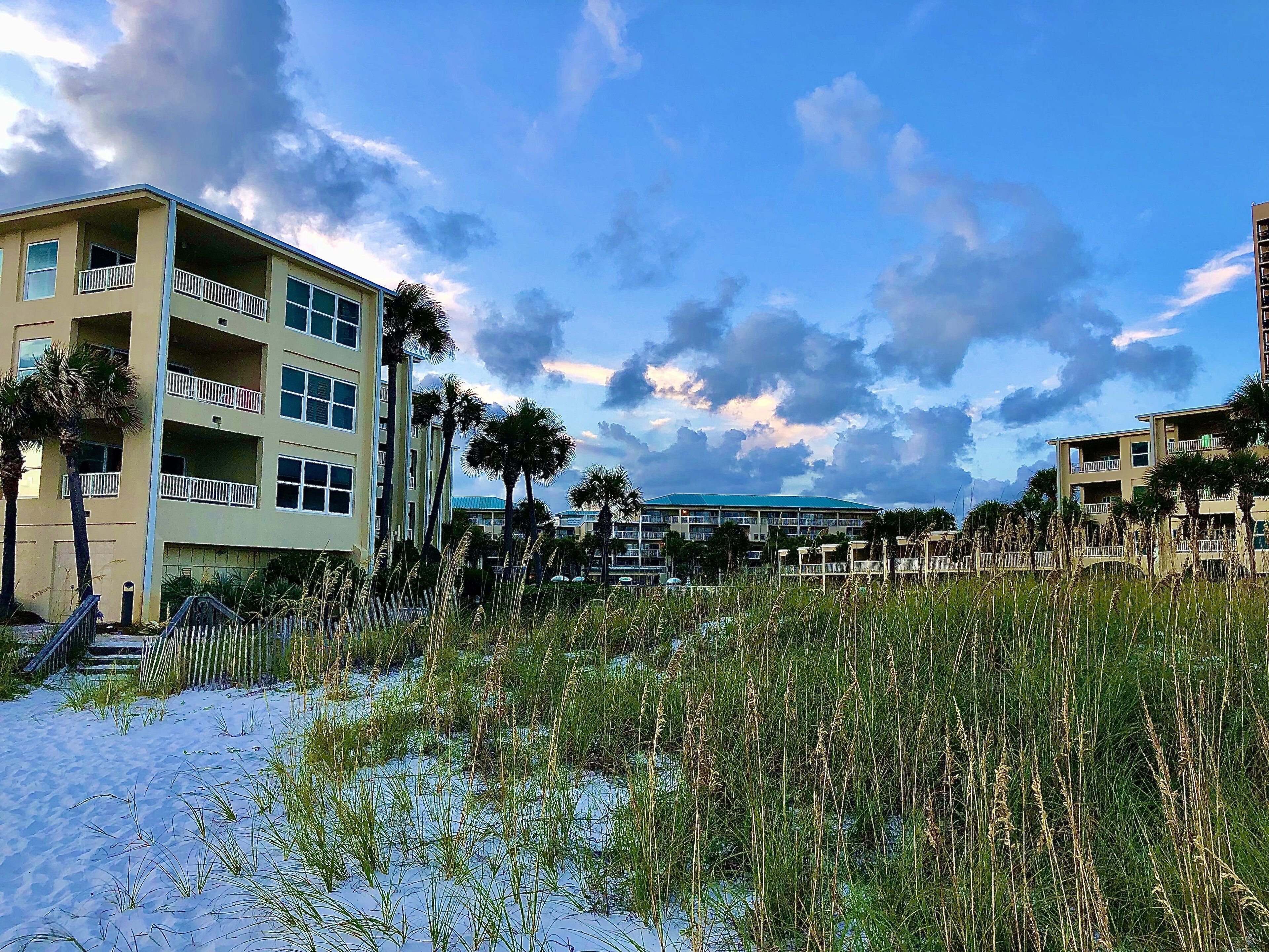 Un hotel frente a la playa con varios pisos, balcones y palmeras.