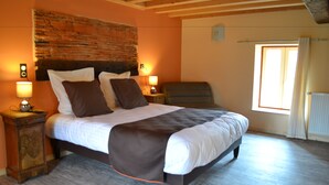 Une chambre avec un mur d’accent en briques, un grand lit recouvert d’une couverture marron, deux lampes de chevet et une fenêtre avec des rideaux.