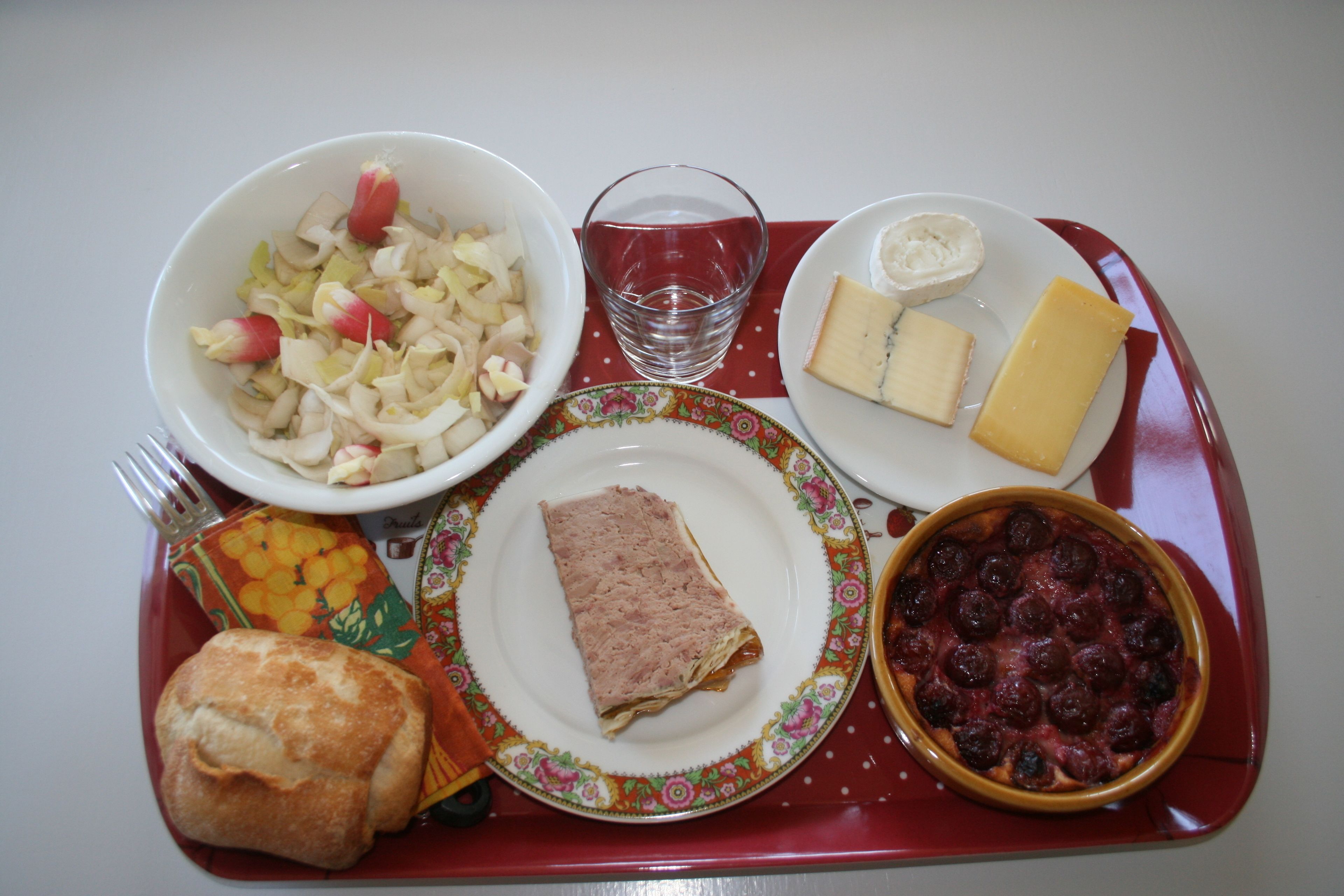Una bandeja con una variedad de alimentos, incluyendo un tazón de ensalada, un plato de queso, una rebanada de carne, un plato al horno y un panecillo.