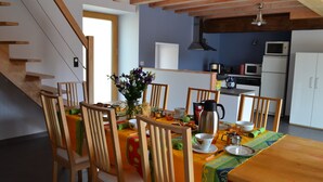 Un coin repas avec des chaises en bois et une table dressée pour le repas, une cuisine en arrière-plan et un escalier menant à l’étage.