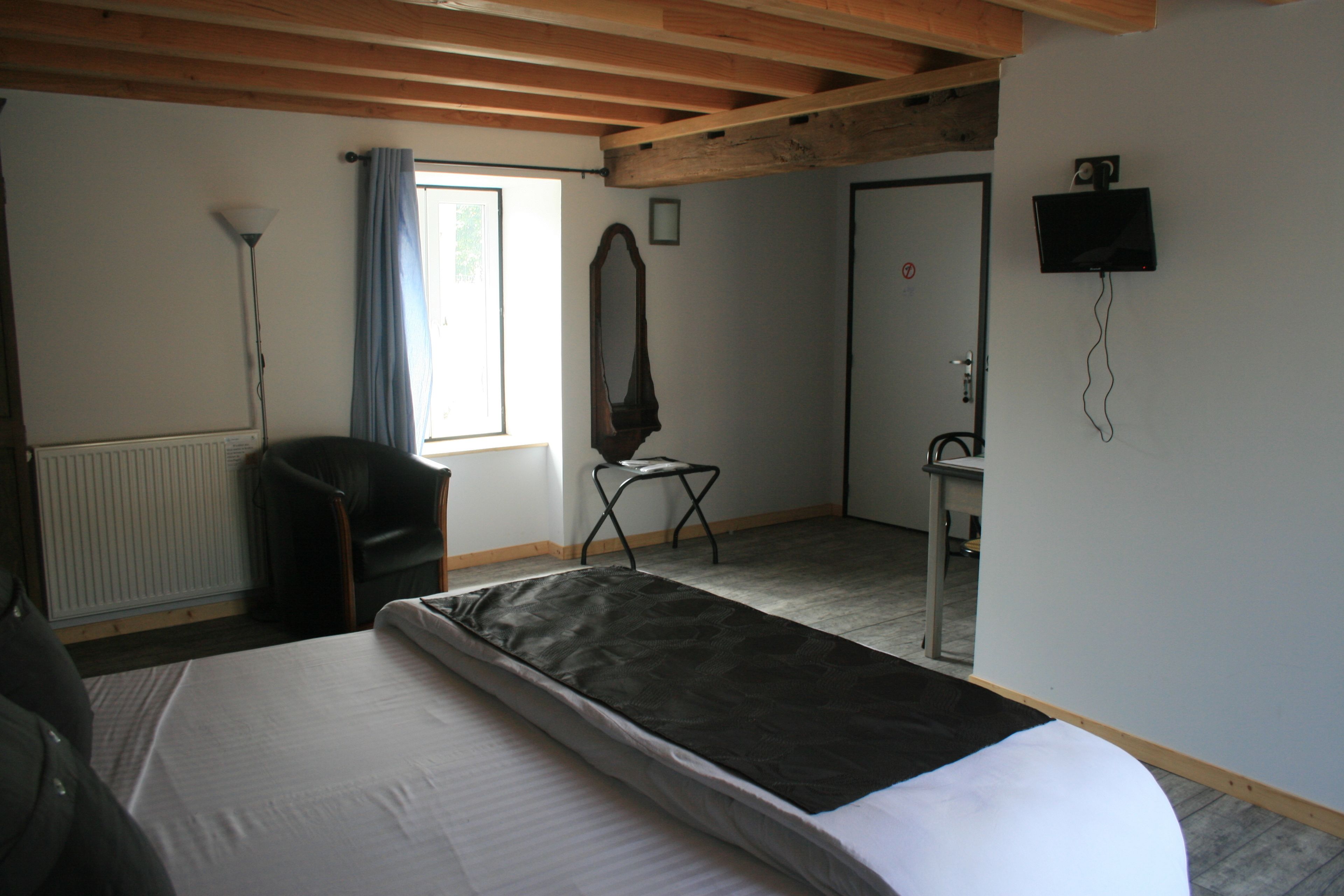 A hotel room with a bed, a chair, a desk, a mirror, a radiator, and a window with curtains.