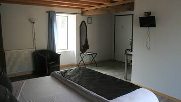 A hotel room with a bed, a chair, a desk, a mirror, a radiator, and a window with curtains.