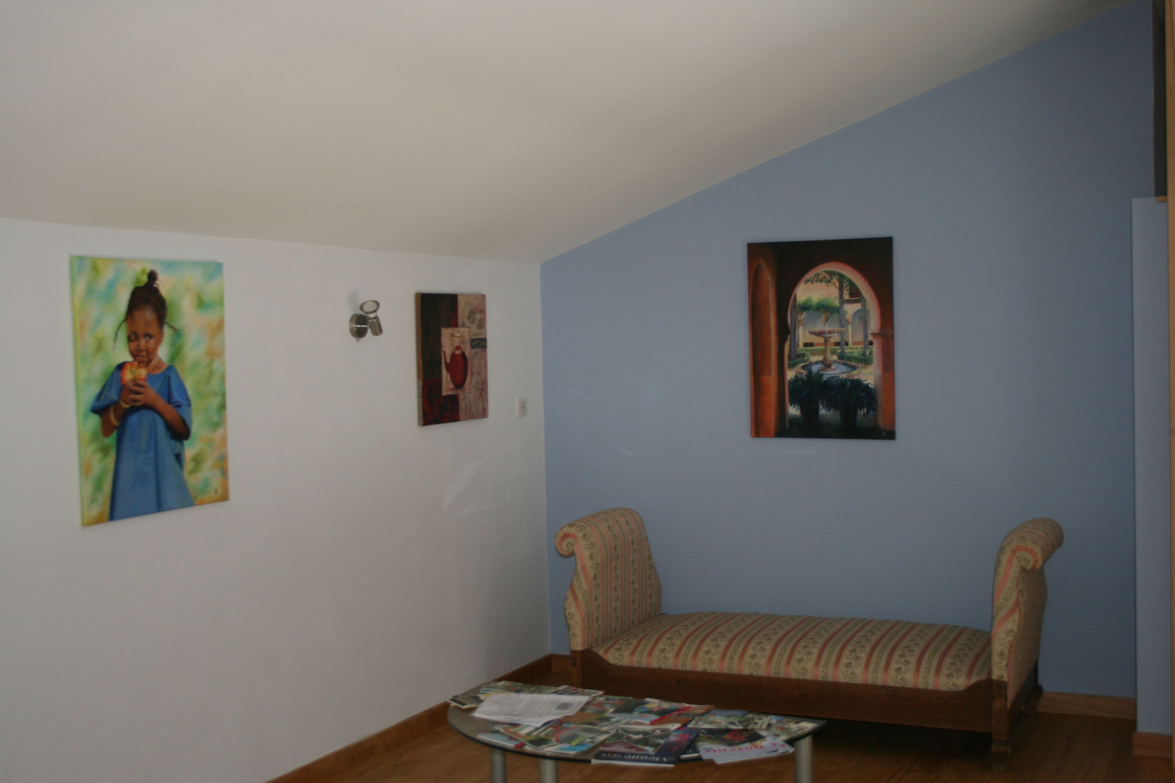 Una habitación con un sofá, una mesita con revistas y tres cuadros en la pared.