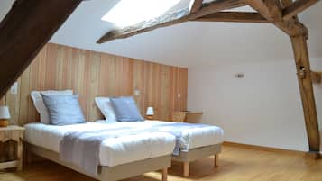 Un dormitorio con techo inclinado, vigas de madera, una cama con almohadas, una mesita de noche con una lámpara y un taburete de madera.
