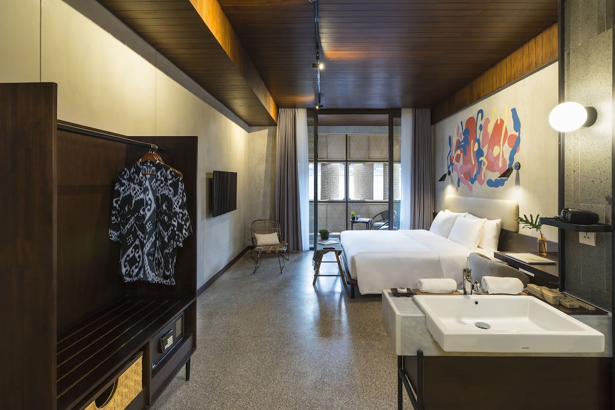 Une chambre d’hôtel comprenant un lit, un bureau, une chaise, une télévision, une armoire et une salle de bain avec un lavabo et un miroir.