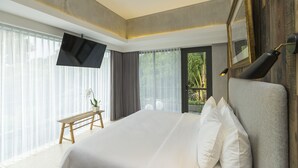 Ein modernes Hotelzimmer mit einem großen Bett, einem Flachbildfernseher, einer Bank und Blick auf Grün hinter dem Fenster.