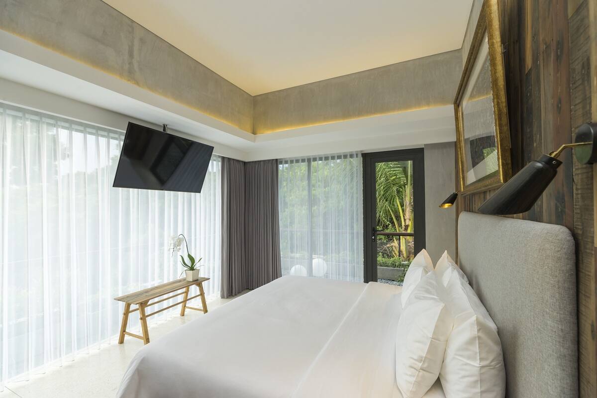 Une chambre d’hôtel moderne dotée d’un grand lit, d’un téléviseur à écran plat, d’un banc et offrant une vue sur la verdure par la fenêtre.