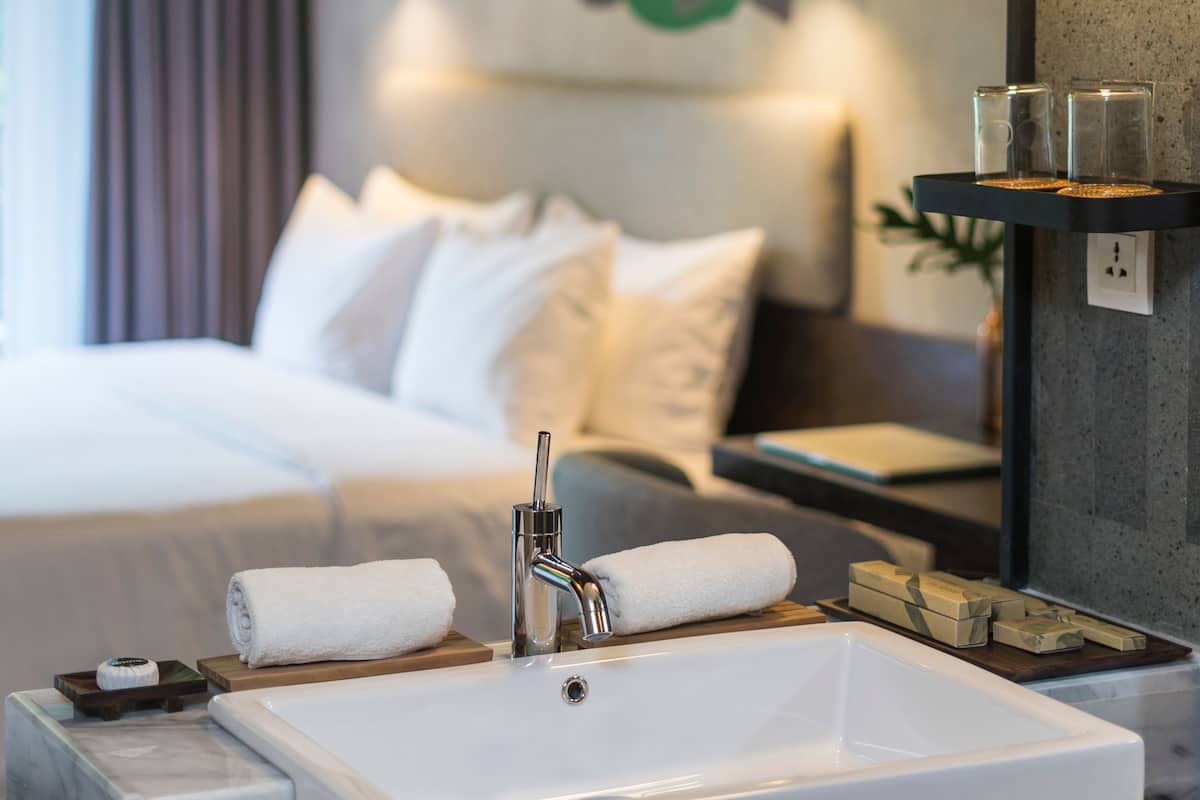 Une salle de bain d’hôtel avec un lavabo blanc, un miroir, une serviette et une étagère contenant des articles de toilette.