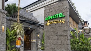 Ein Hotel mit steinverkleideter Fassade, einem Schild mit der Aufschrift "AR+OTEL" und traditionellen Statuen.